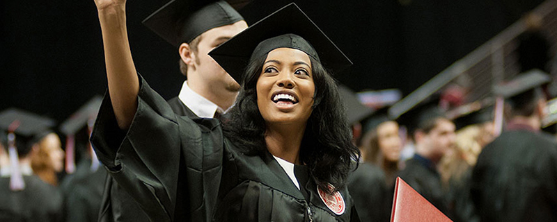 A woman at the Illinois State University graduation ceremony with her degree in hand waving.